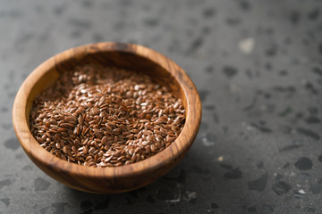 Flax seeds in olive wood bowl on terrazzo surface with copy space