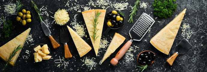 Set of hard cheeses with cheese knives on black stone background. Parmesan. Top view. Free space...