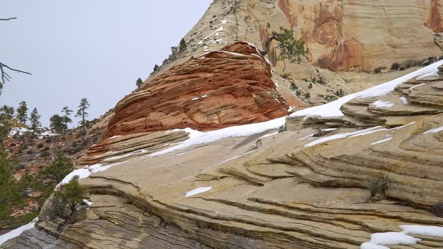 Panning red rock landscape in Zion with snow on the rock layers during winter.