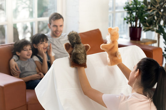 Happy father with cute siblings watching mom puppet show.