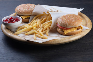 set of burgers on a wooden board. cheeseburger with beef, cheese and vegetables. burger with chicken nuggets, cheese, tomato, cucumber and onions. french fries with ketchup