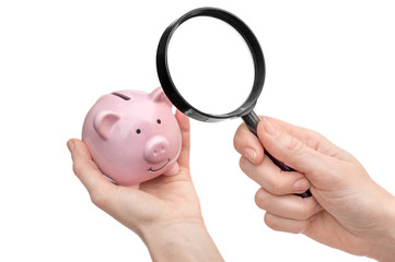 Hand with magnifying glass examining piggy bank on white background. Researching savings.