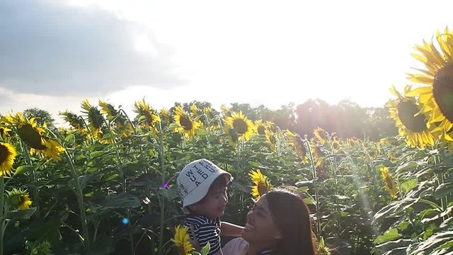 Happy cheerful mother holding his small son high in hands and laughing in sunflower field. Attractive woman holding a little boy in her arms in a field with sunflowers.
