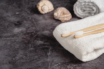Dental care and Eco friendly and reuse concept. Two eco natural bamboo toothbrushes, seashell, white towel on grey background. Sustainable lifestyle and zero waste home. Copy space