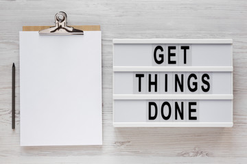 'Get things done' words on a modern board, clipboard with blank sheet of paper on a white wooden background, top view. Overhead, from above, flat lay.
