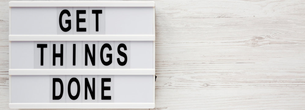 'Get things done' words on a lightbox on a white wooden surface, top view. Overhead, from above, flat lay. Space for text.