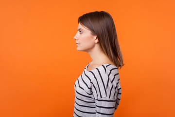 Side view portrait of calm confident young woman with brown hair in long sleeve striped shirt...