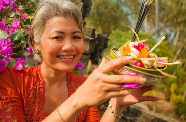 beautiful and happy Asian Indonesian woman dressed in traditional Balinese religious custom holding...
