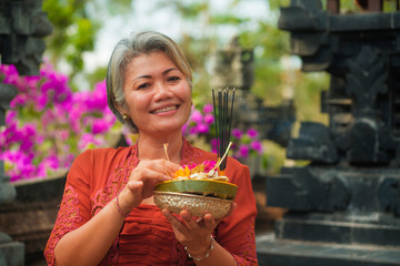 beautiful and happy Asian Indonesian woman dressed in traditional Balinese religious custom holding...