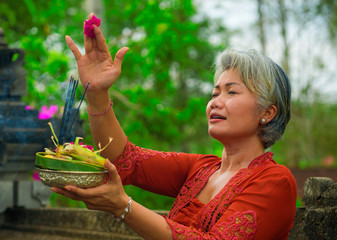 beautiful and happy Asian Indonesian woman dressed in traditional Balinese religious custom holding...
