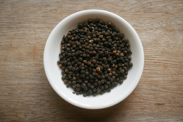 Black pepper in a white plate on wooden background. 