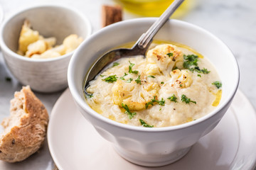 Roasted cauliflower cream soup on white kitchen table, served with fresh parsley, olive oil and...