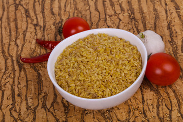 Raw bulgur in the bowl with tomatoes and garlic