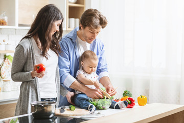 Cute baby boy preparing vegetable salad with parents at kitchen