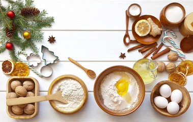 Cooking dough for sweet Christmas treats. Bowl with flour, eggs, nuts, spices, oil, sugar and branches of a decorated Christmas tree on a white table. Flat lay, copy space, close-up, mock up