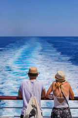 Tourists with a straw hat stand on the deck of a cruise ship and look out over the ocean  While the...