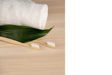 Zero waste concept. Eco natural bamboo toothbrush, white frame and towel on wooden background with green leaf. Plastic free essentials, teeth care. Sustainable lifestyle