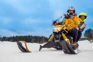 Riding a snowmobile. Two people ride a snowmobile. Pair races on snowmobiles. Extreme sports. Riding through snowdrifts. Winter sports. Man and a woman are resting together. Car for moving in snow.