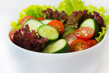 Fresh vegetable salad on white background close. Dinner of lettuce, tomatoes and cucumbers.