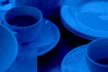 Two tea or coffee cups on wooden table surrounded by dishes, Selective focus. Reastaurant, cafe, breakfast, tableware. Horizontal. Classic, blue monochrome, trend 2020