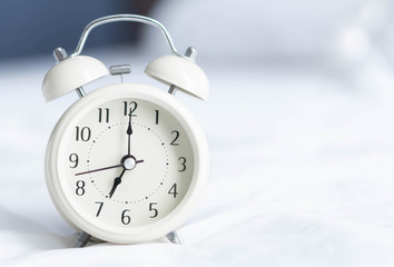 Alarm clock on wooden table for wake up time with light from window, selective focus