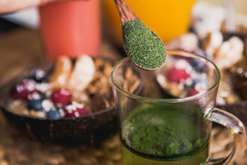 Chlorella powder above glass with healthy breakfast in the background