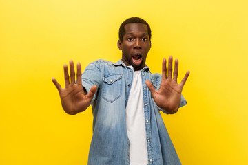 Portrait of frightened hysterical young man in denim casual shirt standing with open mouth and...