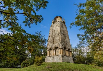 Zelena hora, Pelhrimov / Czech Republic - September 13 2019: Bismarck tower made of stone standing in the woods close to Cheb on a sunny day with blue sky. Green grass and trees around.