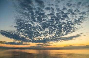 Amazing beautiful peaceful sunrise or sunset tropical landscape. Fluffy clouds moving in blue sky, golden gradient sunny horizon line and shiny surface of sea water. Horizontal color photography.