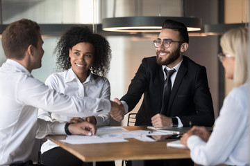 Smiling diverse business partners handshake greeting at meeting