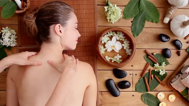 Top view of young relaxed woman is lying and resting on couch in ayurveda salon. Girl is taking thai massage. Hands of master are massaging female back and shoulders. Spa and relax concept.