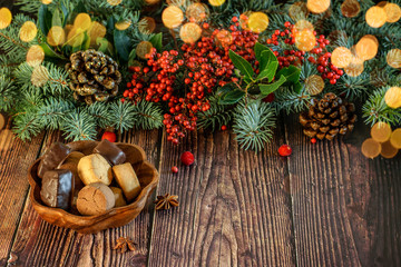 Christmas and New Year vignette of branches of blue fir, pinecones and red berries with a plate of cookies on the wooden natural background.