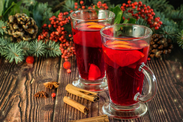 Hot traditional drink Mulled wine on the wooden brown background closeup. Christmas and New Year vignette of branches of blue fir, pinecones and red berries. Holidays decoration with lights.