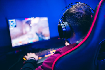 Professional gamer playing online games tournaments pc computer with headphones, Blurred red and blue background © Parilov