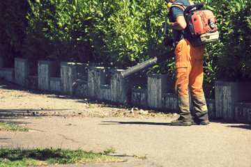 Manual worker on the street, road sweeper using a leaf blower