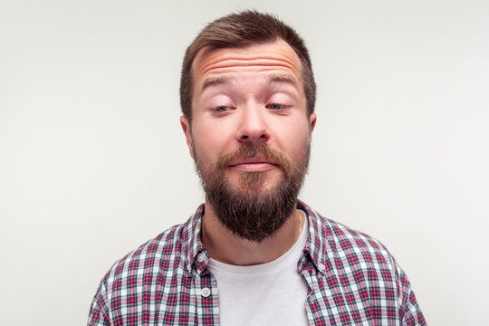 Portrait of funny awkward bearded man in casual plaid shirt standing with crossed eyes, comic silly expression, looking carefree and dumb, making faces. studio shot isolated on white background