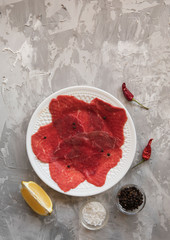 Marble beef carpaccio with lemon, olive oil and Parmesan cheese on background with plaster texture....