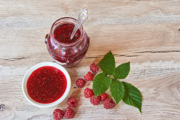 Raspberry jam and fresh raspberry with green leves on a rustic wooden table