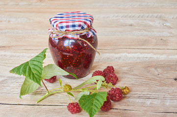 Raspberry jam and fresh raspberry branch on a rustic wooden table
