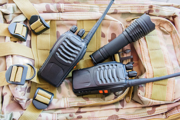 Equipment for trekking. Set of traveler or tourist or soldier. Radio for communication, flashlight on the background of a military backpack camouflage