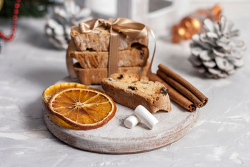 Traditional Italian biscotti or cantuccini cookies on a round white wooden board with cinnamon, dried orange slices and marshmallows on a light background with pine cones. Christmas baking concept