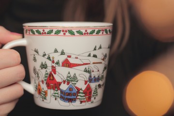 Closeup of a woman holding a Christmas cup with fairy lights in the foreground.