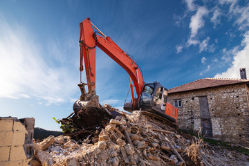 A heavy industrial work machine, digger is destroying an abandoned old building 