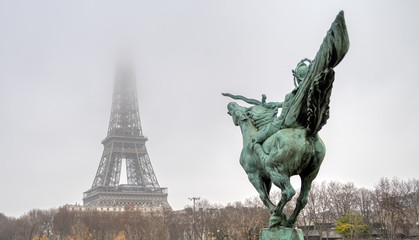 Top of the Eiffel Tower lost in the mist with Bir-hakeim statue La France Renaissante in foreground...