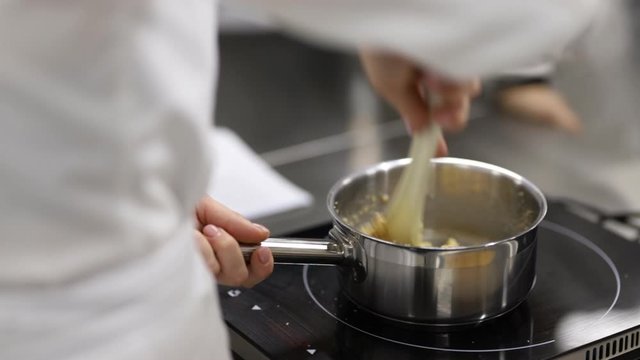 A pastry chef in a white uniform heats the sauce in a saucepan on an induction cooker