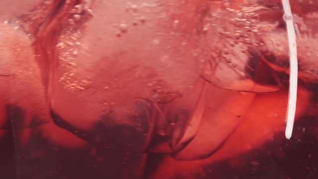 Wine coctail with ice in a glass. Red wine coctail pouring in a glass over blue background. Rose wine pour into a glass. Close up shot. Slow motion 