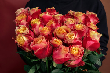 young woman in a black jacket embraces a bouquet of large roses