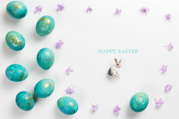 Happy easter card. Stylish minimalistic composition of turquoise with gold easter eggs on a white background. Figurine of a rabbit and delicate spring flowers. Flat lay, top view, copy space