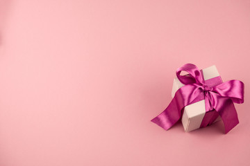 top view gift box with festive satin ribbon bow on a soft pink background with copy space