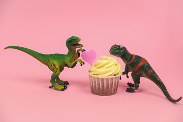 cute green plastic dinosaur toys with cupcakes decorated with pink heart on a pastel pink background © dvulikaia